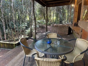 Un patio al aire libre con una mesa redonda de vidrio y sillas de mimbre, rodeado por una pérgola de madera y un muro de ladrillo.
