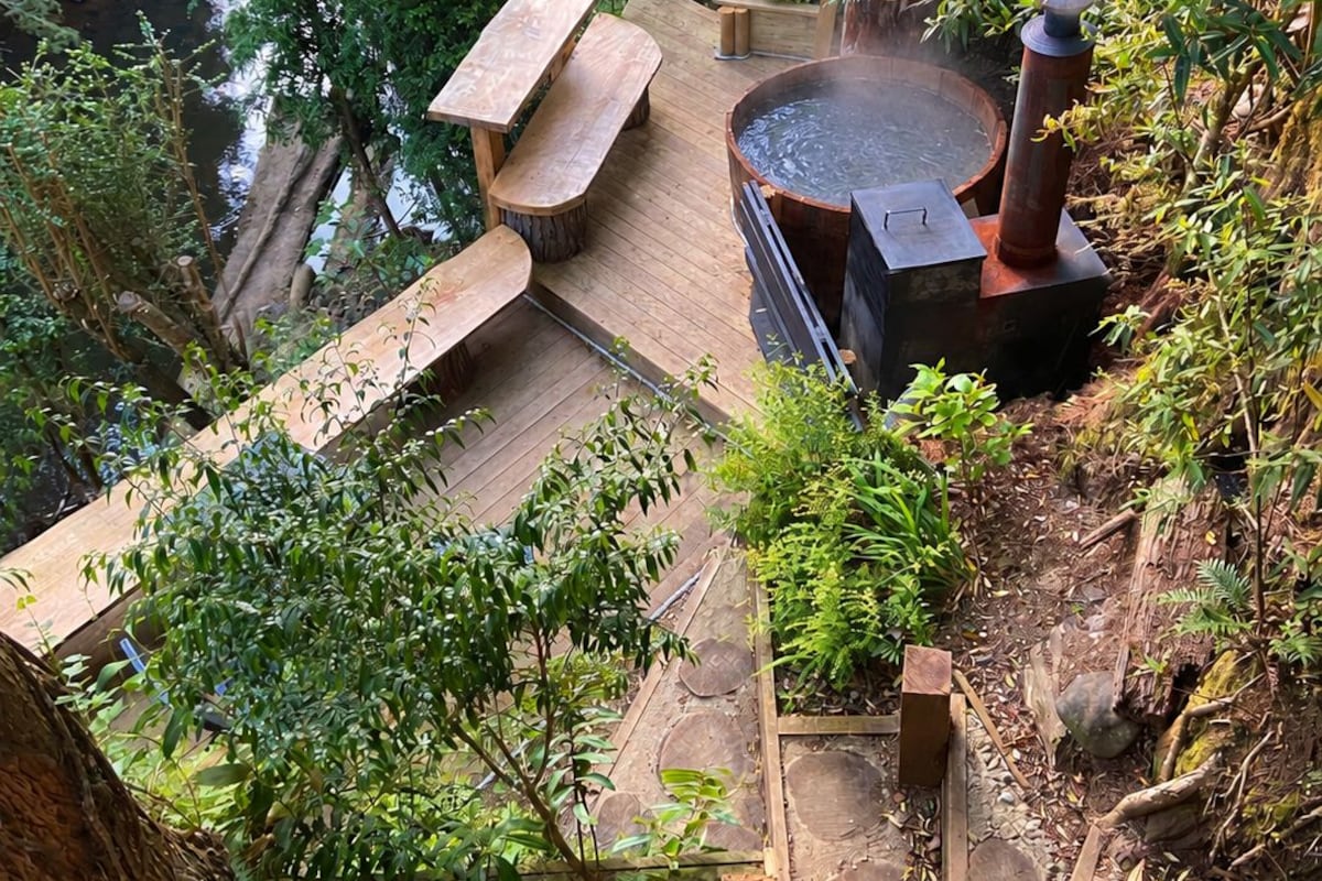 A wooden deck with a hot tub surrounded by lush greenery and a small waterfall.