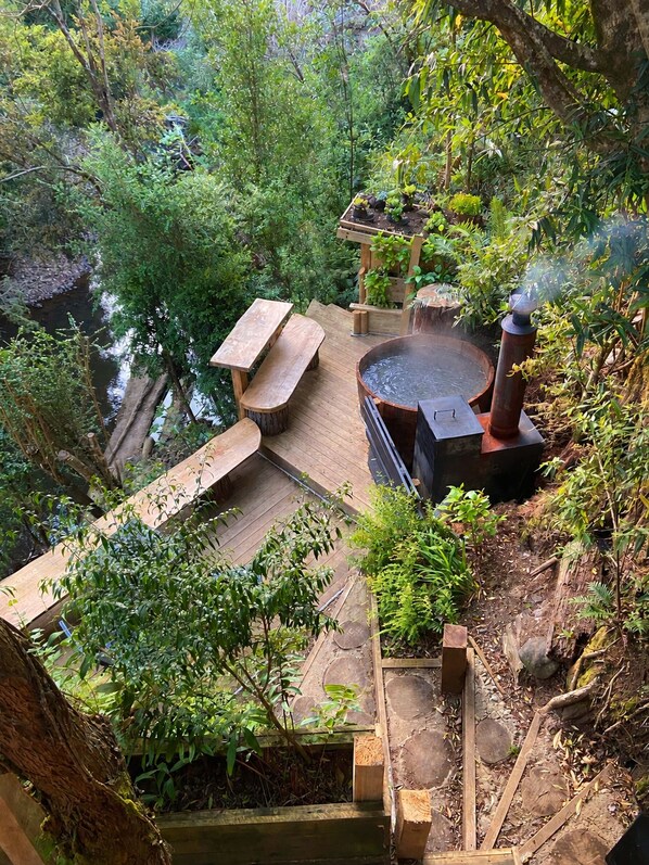 A wooden deck with a hot tub surrounded by lush greenery and a small waterfall.