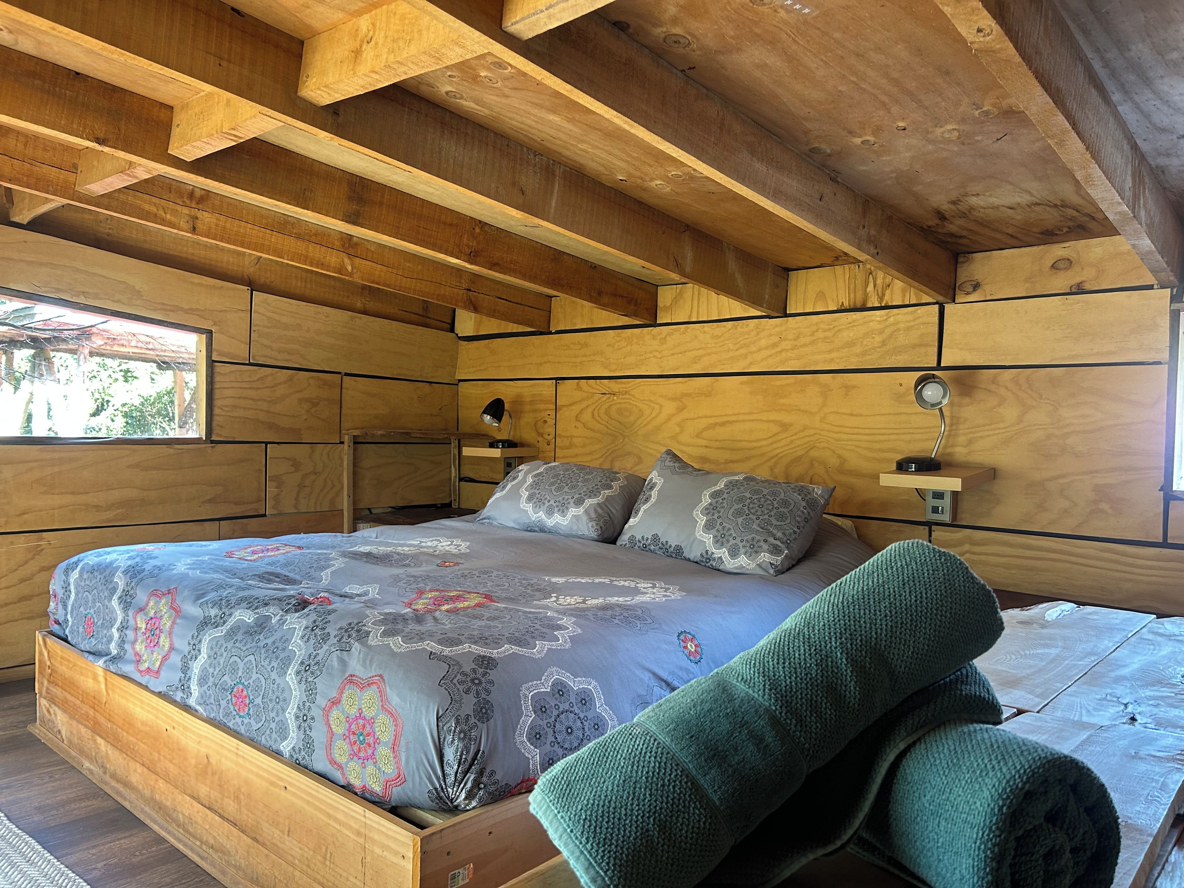 A wooden bedroom with a bed, pillows, a nightstand, and a window.