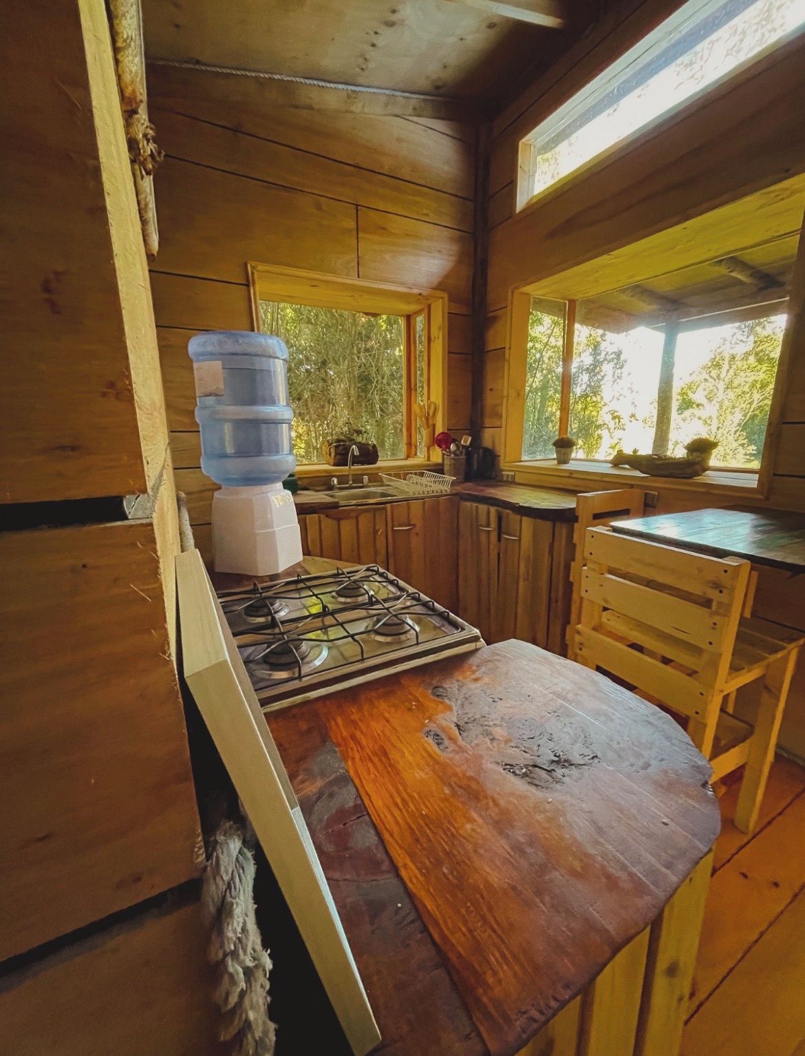 A wooden cabin kitchen with a gas stove, wooden cabinets, a window, and a water dispenser.