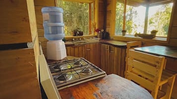 A wooden cabin kitchen with a gas stove, wooden cabinets, a window, and a water dispenser.