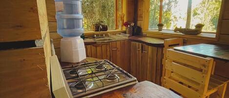 A wooden cabin kitchen with a gas stove, wooden cabinets, a window, and a water dispenser.