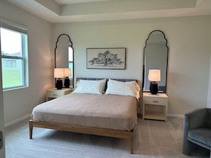 Une chambre à coucher avec un lit, deux tables de chevet, deux lampes, un miroir et un tableau encadré accroché au mur.