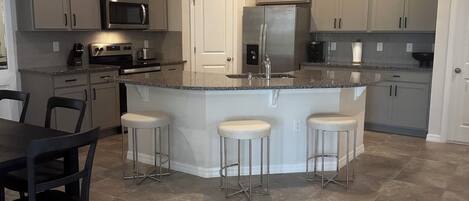 Cozinha moderna com ilha central, banquetas e área de jantar com mesa e cadeiras.