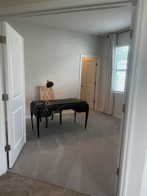 A room with a carpeted floor, a black table, a chair, and a door. - Ocala Perserve Villa (Ocala)