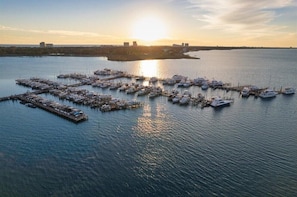 An aerial view of a marina with numerous boats docked at piers, surrounded by calm water and a distant shoreline with buildings. - Alluring 2BR/2BA With Spectacular Baytowne Fireworks View (Miramar Beach)