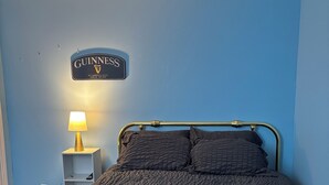 Quarto de hotel com uma cama, mesa de cabeceira com abajur e placa na parede.
