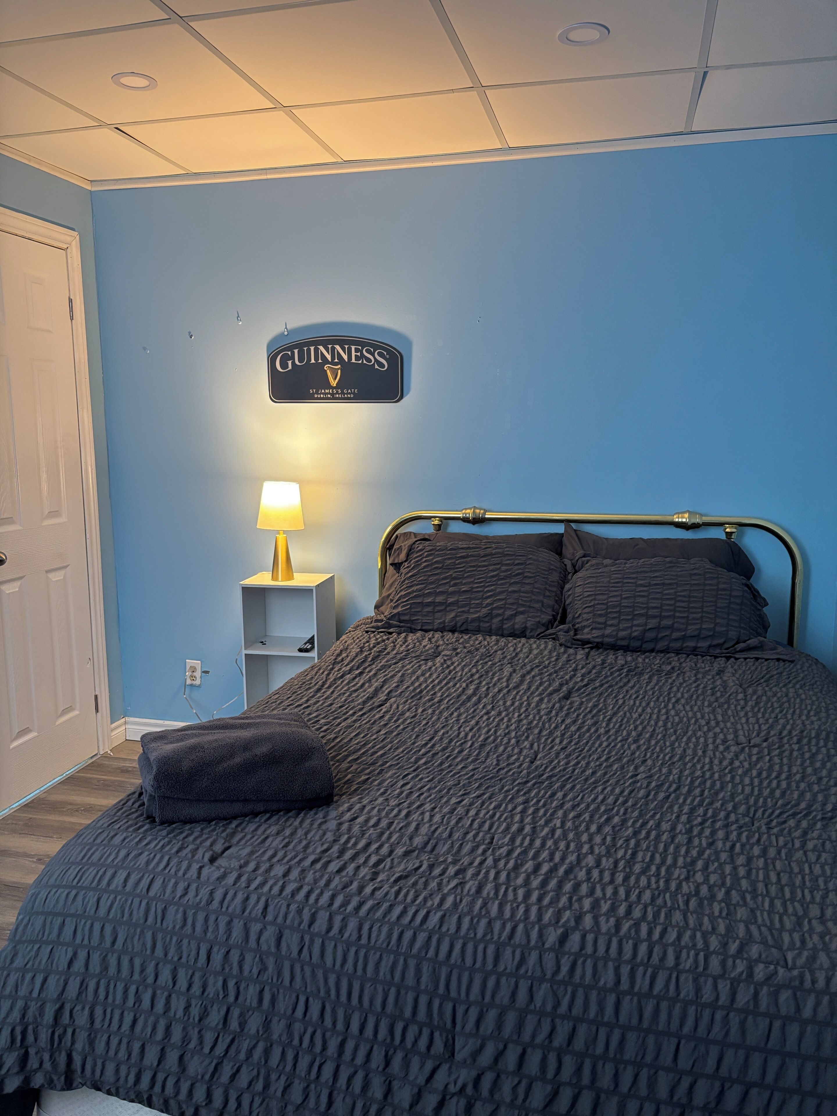 A bedroom with a bed, a nightstand with a lamp, and a wall sign.