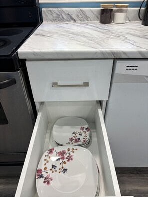 A kitchen with a white countertop, a stove, and a drawer with a floral plate.