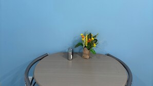 Uma mesa redonda com uma cadeira de metal, uma placa emoldurada na parede e uma pequena planta florida.