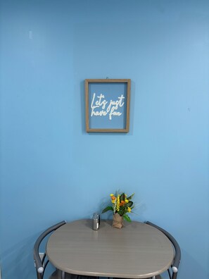 A round table with a metal chair, a framed sign on the wall, and a small plant with flowers. - 1 Bedroom Apartment in Motel, 4 minutes walk to the beach (Saugeen Shores)