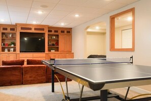 A room with a ping pong table, wooden cabinets, a flat-screen TV, and a mirror. - Spacious 3BR Family Home | Bunks + Ping Pong (Peoria)