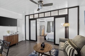 A modern living room with a sofa, a coffee table, and a TV. There is a wooden cabinet and a ceiling fan. - Delightful 1-bedroom apartment in Singer Island with Pool and Beach access (Riviera Beach)