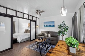 A modern living room with a bed, sofa, coffee table, and a painting of sailboats. - Delightful 1-bedroom apartment in Singer Island with Pool and Beach access (Riviera Beach)