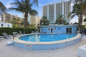Una piscina con un letrero que indica un límite de profundidad de 1.8 metros, rodeada de sillas de descanso y palmeras.