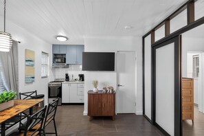 A modern kitchen with white cabinets, a microwave, and a stove. There is a dining area with a wooden table and chairs. - Delightful 1-bedroom apartment in Singer Island with Pool and Beach access (Riviera Beach)