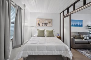 Un dormitorio con cama, sofá, un cuadro y una ventana con cortinas.