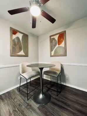 A corner room with a ceiling fan, two abstract paintings, a round table, two chairs, and dark wooden flooring. - Comfortable 2BR Retreat - 1st Floor Living (Waxahachie)