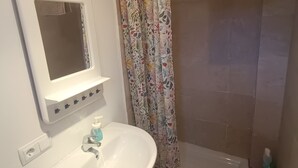 Un bagno con un lavandino bianco, uno specchio, una doccia con tenda a fiori e un asciugamano appeso al muro.