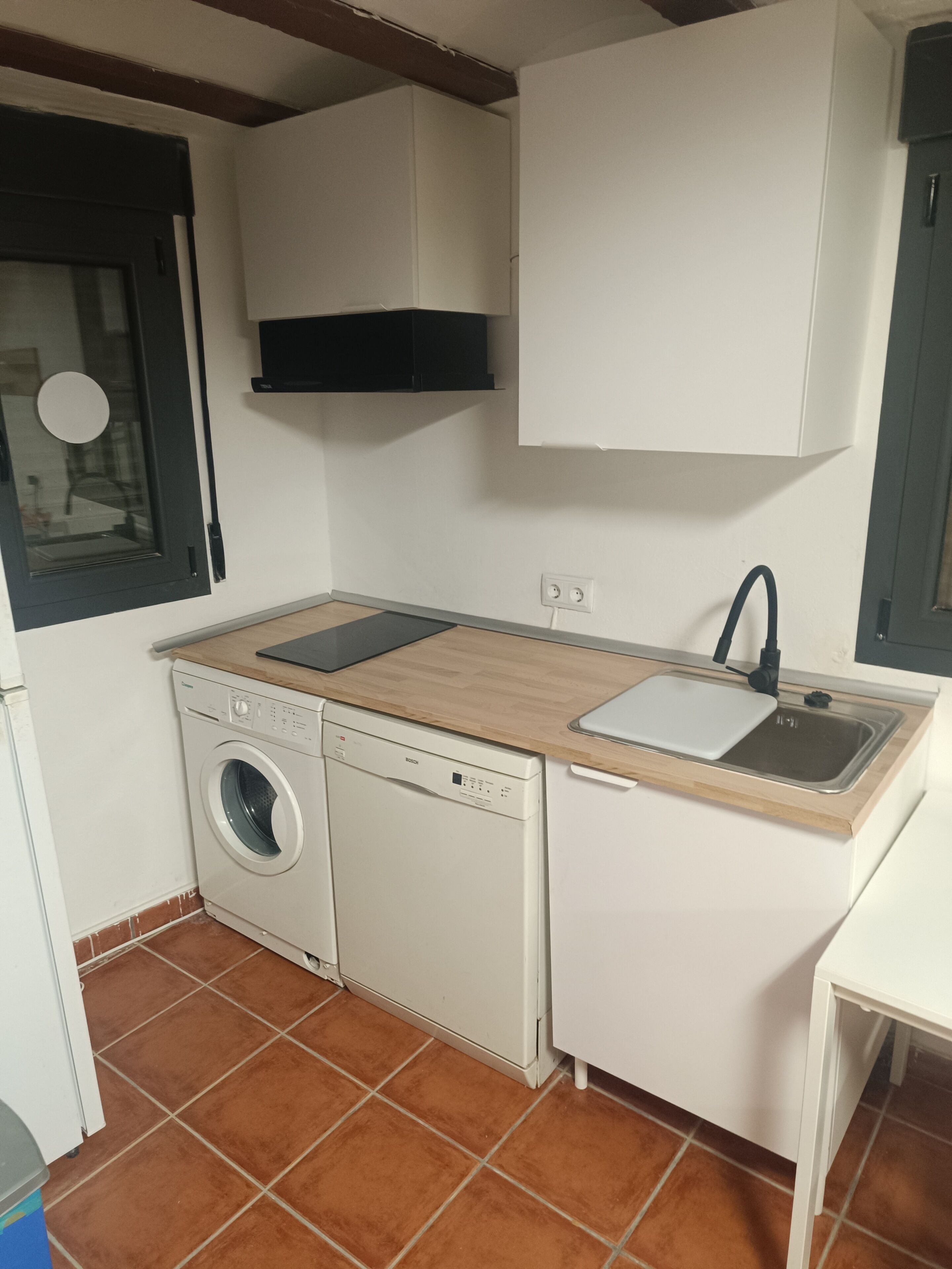 Een praktische keuken met een wasmachine, een spoelbak en een houten aanrecht.