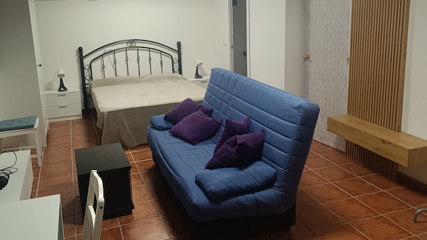 A room with a bed, a blue sofa, a desk, and a chair. - Azafrán Apartment (Blancas)
