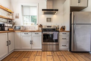 A modern kitchen with white cabinetry, stainless steel appliances, and a wooden floor.