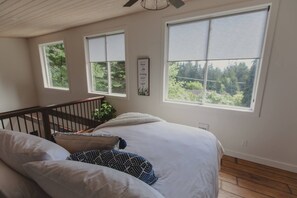 A bedroom with a large bed, two windows, a ceiling fan, and a staircase.