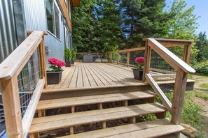 A wooden deck with steps leading to a house, surrounded by greenery.