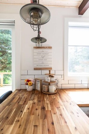 A kitchen with a wooden countertop, a hanging light fixture, a welcome sign, and a window with a view of greenery.