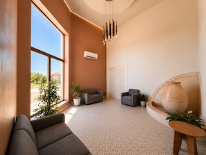A modern interior with a geometric patterned floor, a grey sofa, two armchairs, a potted plant, and a unique sculptural piece. - Magnolias Suites Hotel (Nuevo Casas Grandes)