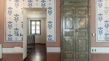 A hallway with patterned wallpaper, a wooden door, and a staircase leading to another room.