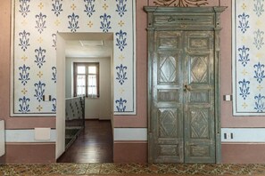 A hallway with patterned wallpaper, a wooden door, and a staircase leading to another room.