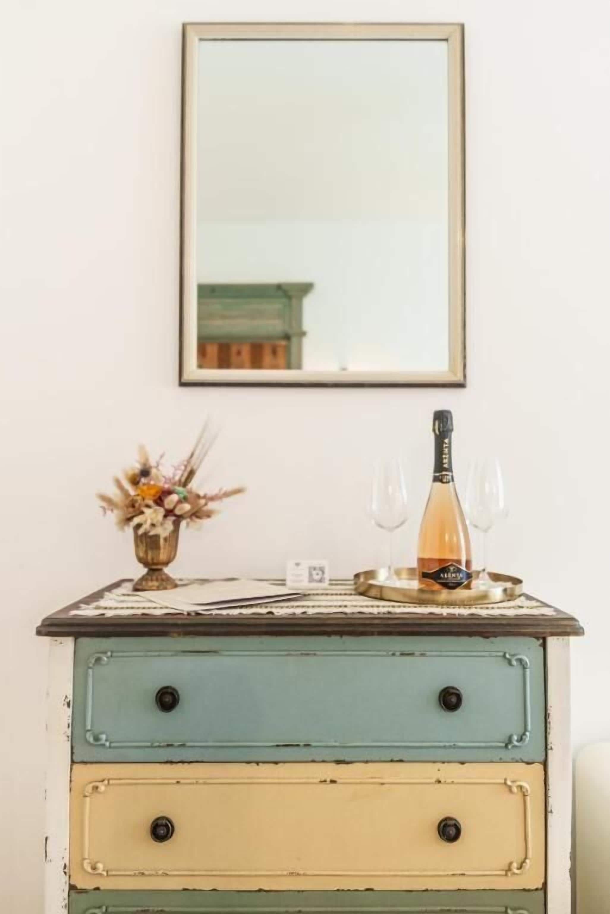 A vintage dresser with a mirror above it, a bottle of wine, and a glass on the dresser.