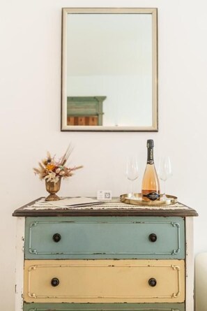 A vintage dresser with a mirror above it, a bottle of wine, and a glass on the dresser.