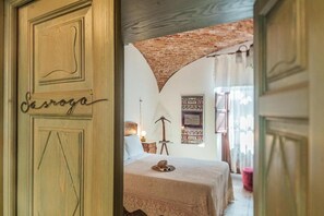 Una habitación con una cama, un sombrero sobre la cama, una lámpara y una pared con un cuadro.