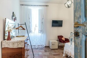 A room with a bed, a TV mounted on the wall, a red chair, a small table with a vase, and a curtain with a pattern.