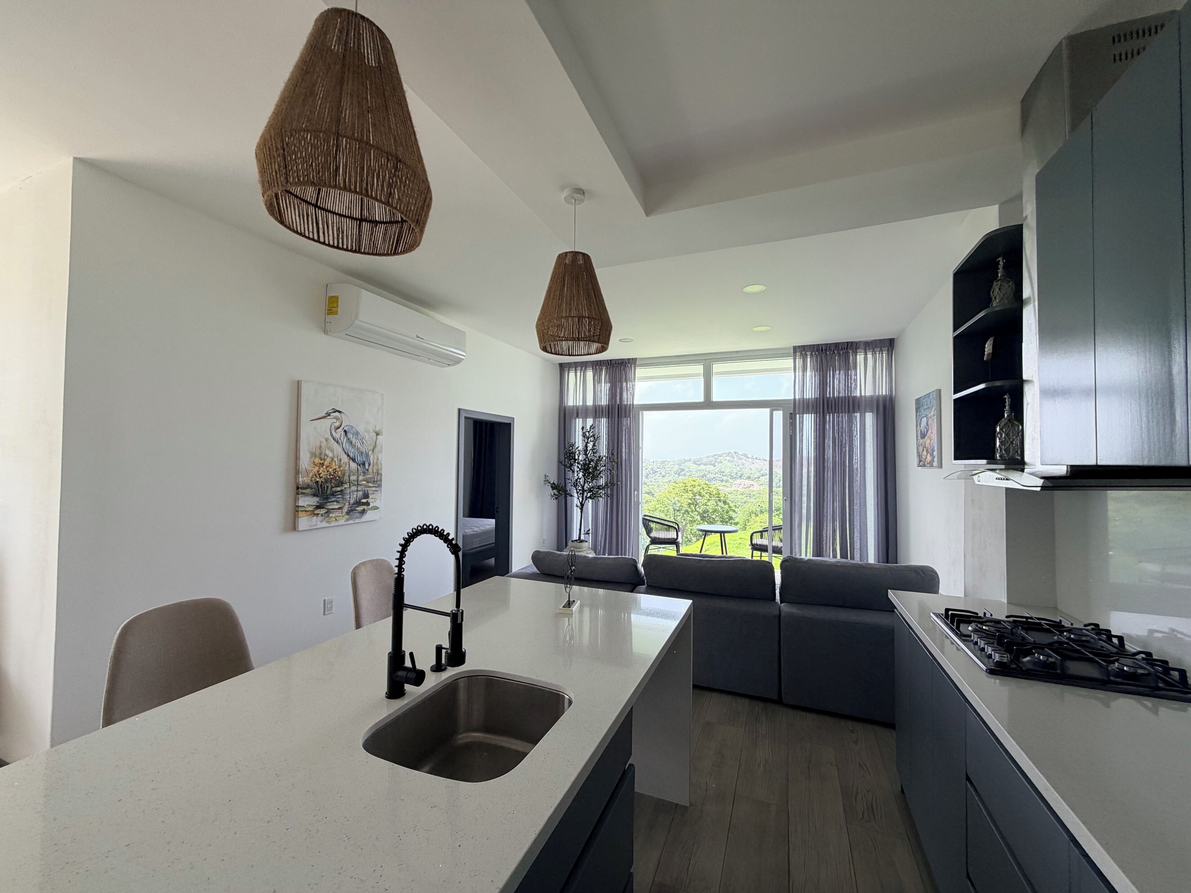 A modern kitchen with a central island, a dining area with a sofa, and a view of the outdoors.