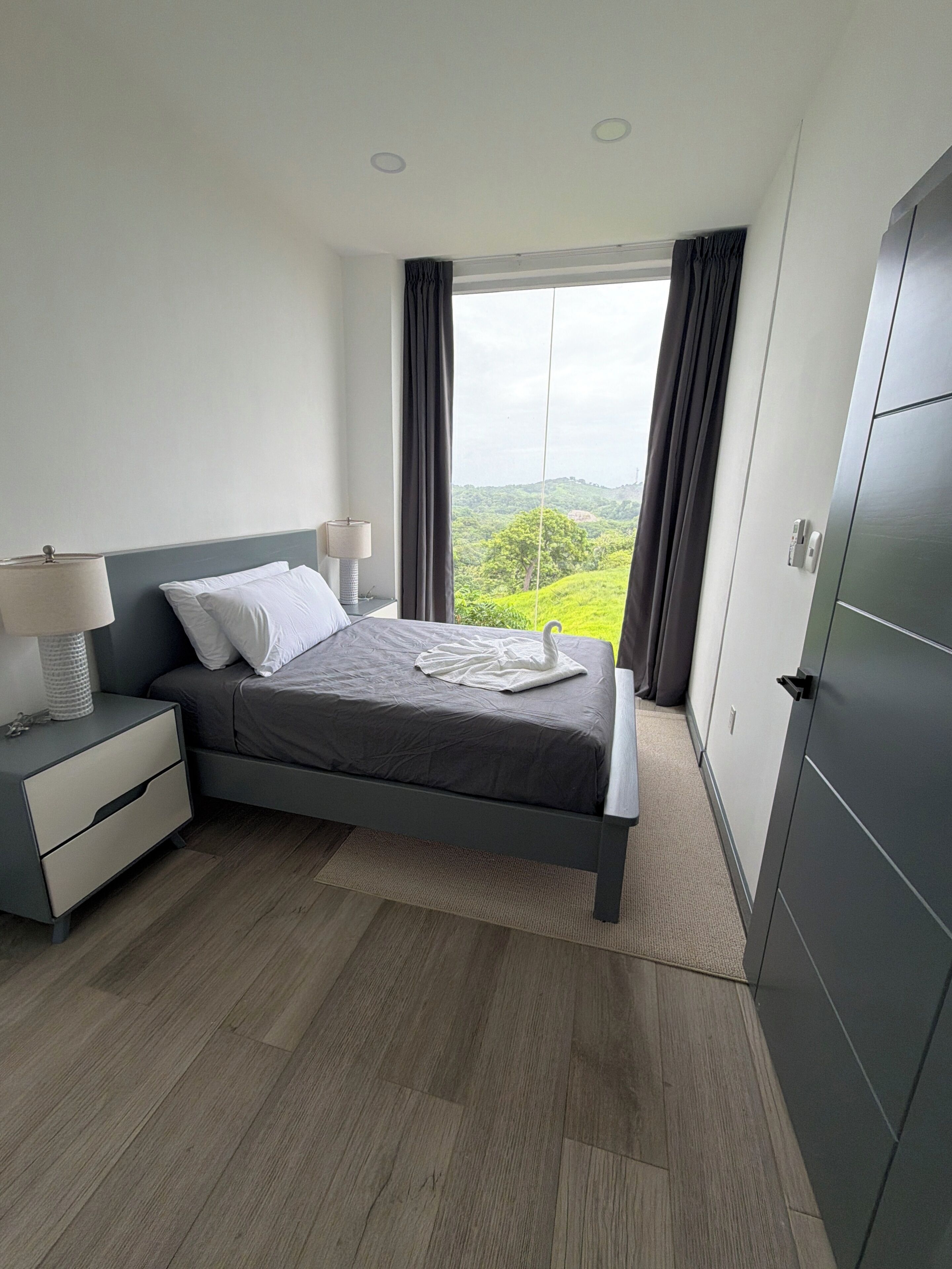 Un dormitorio moderno con cama, mesitas de noche y vistas al verdor.