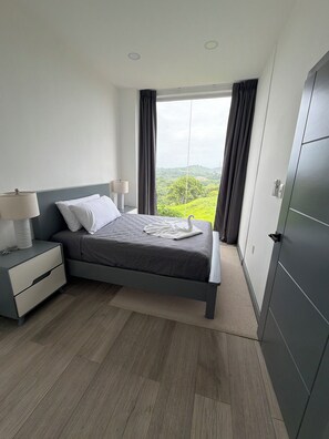 A modern bedroom with a bed, bedside tables, and a view of greenery.