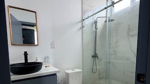 Ein modernes Badezimmer mit Duschkabine aus Glas, einer weißen Toilette und einem dunkel gefärbten Waschtisch mit schwarzem Waschbecken.