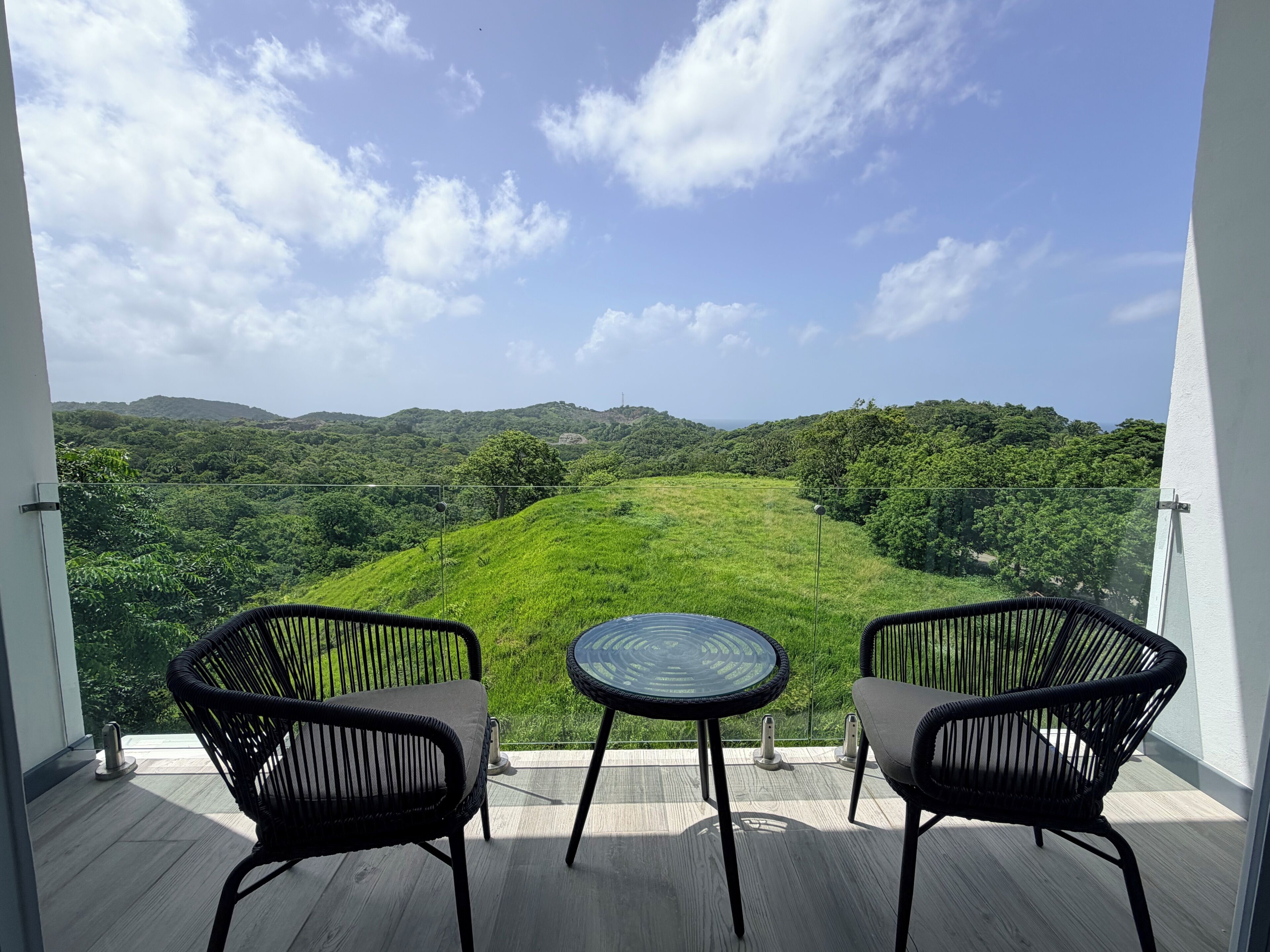 Ein Balkon mit zwei Korbstühlen und einem kleinen runden Tisch, mit Blick auf eine üppige, grüne Landschaft mit Hügeln.
