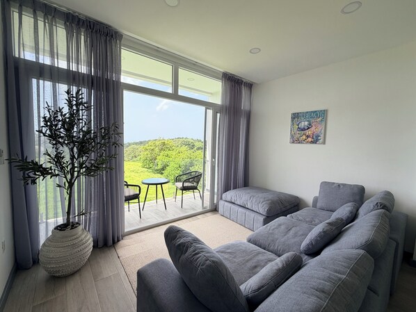 A modern living room with a grey sofa set, a potted plant, and a view through large windows.