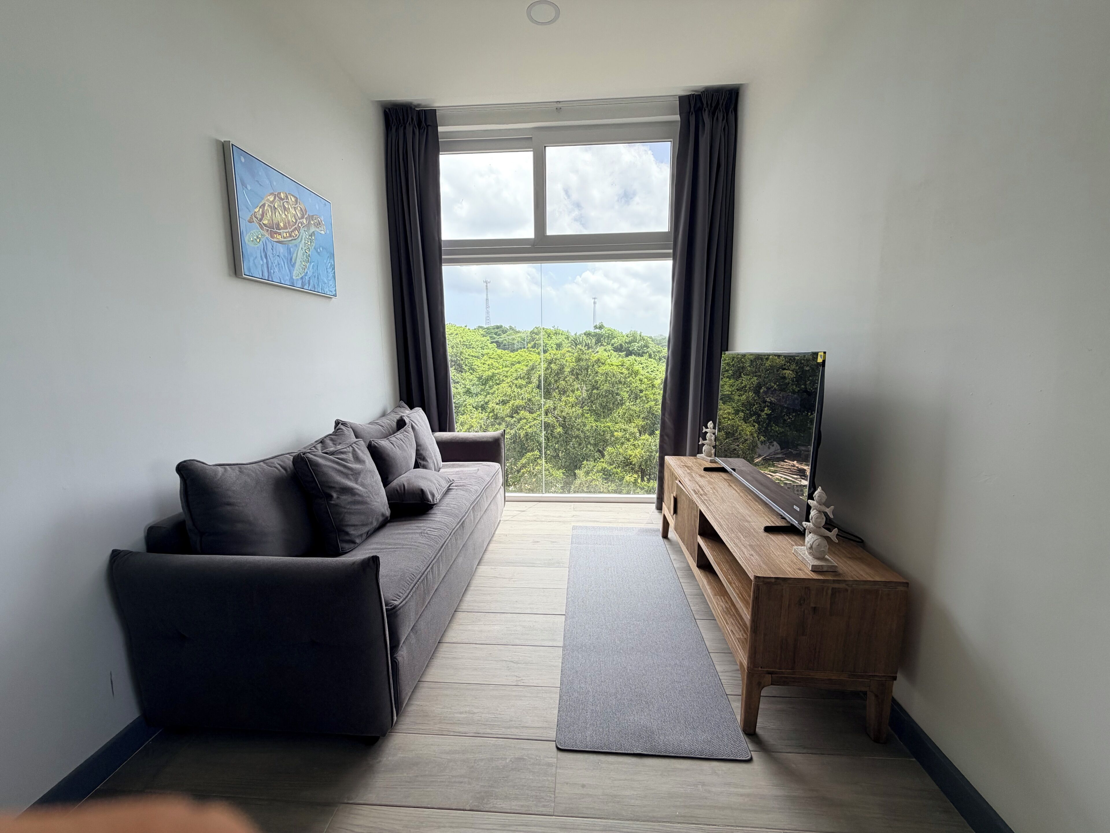 A modern living room with a sofa, a wooden side table, and a large window with curtains.