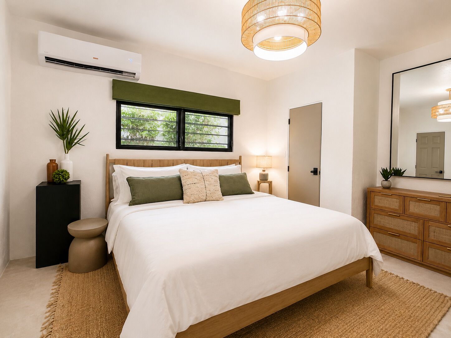 Een slaapkamer met een bed, nachtkastjes, een spiegel, een dressoir, een airconditioning en een raam met uitzicht op groen.