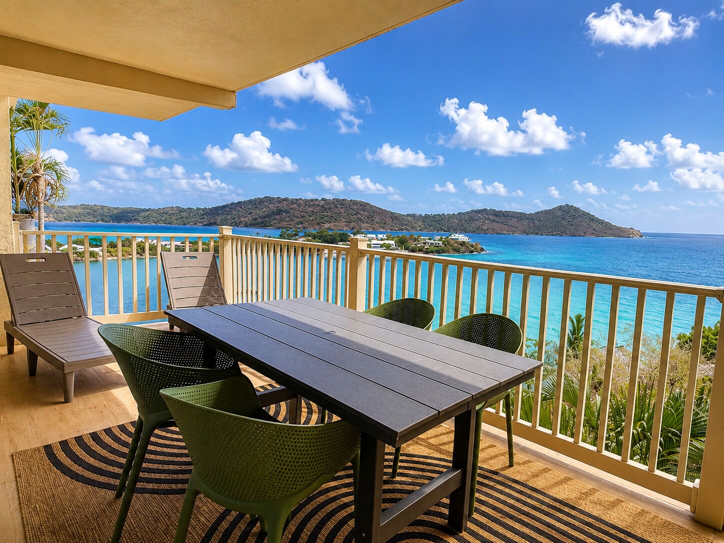 A balcony with a table and chairs, overlooking a coastal view with clear skies.