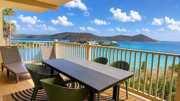 A balcony with a table and chairs, overlooking a coastal view with clear skies.