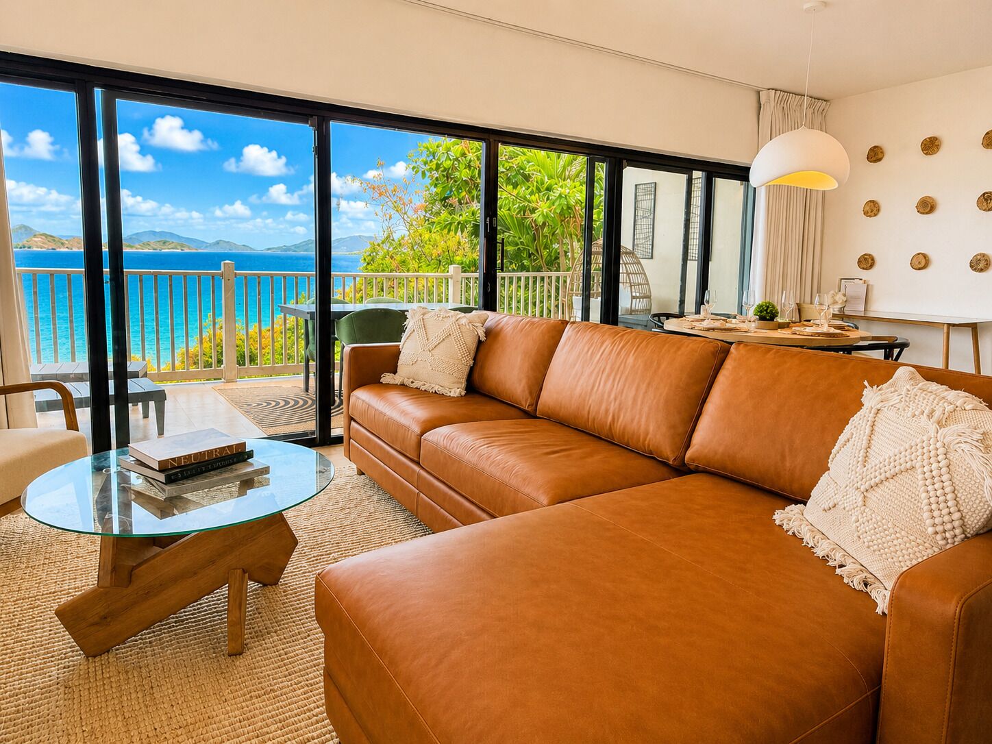 Un salon moderne avec un canapé en cuir, une table basse en verre et une vue sur la mer grâce à de grandes fenêtres.
