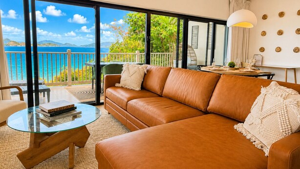 A modern living room with a leather sofa, a glass coffee table, and a view of the sea through large windows. - Panoramic Caribbean views at Villa Orizzonte (St Thomas)