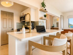 A modern kitchen with a central island, bar stools, a microwave, and a laptop.